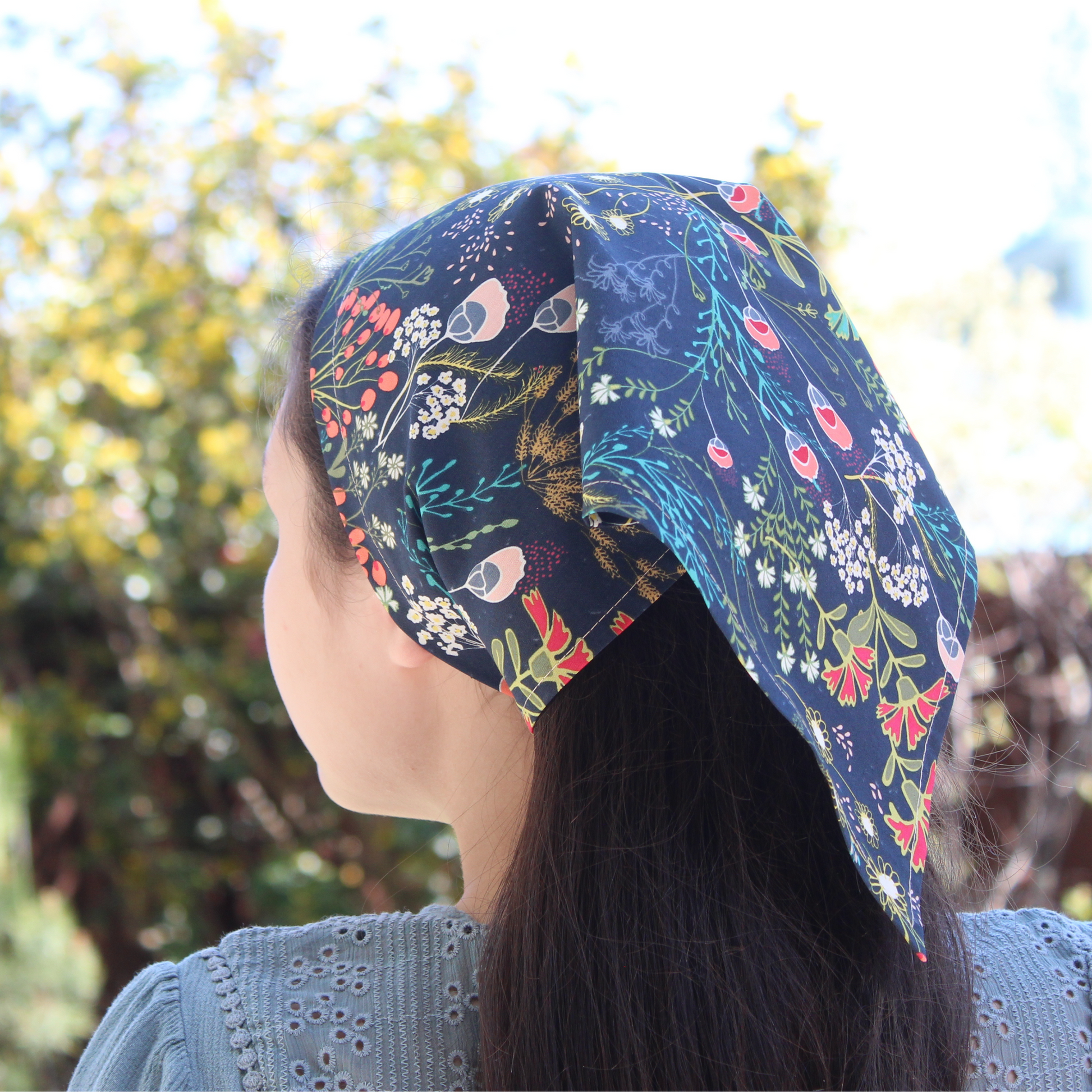 Person wearing a colorful floral patterned headscarf outdoors with trees in the background