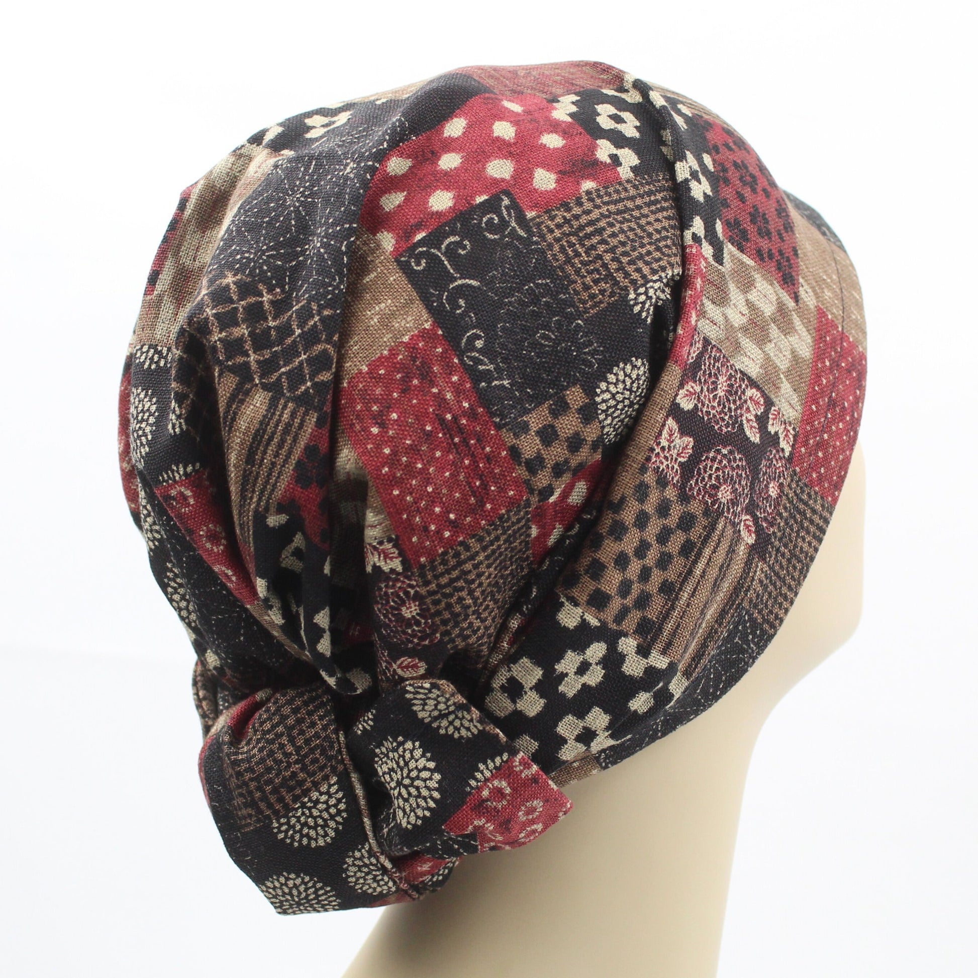 A mannequin head showcasing a multicolored patchwork fabric hair wrap, featuring a mix of burgundy, brown, and black patterns.