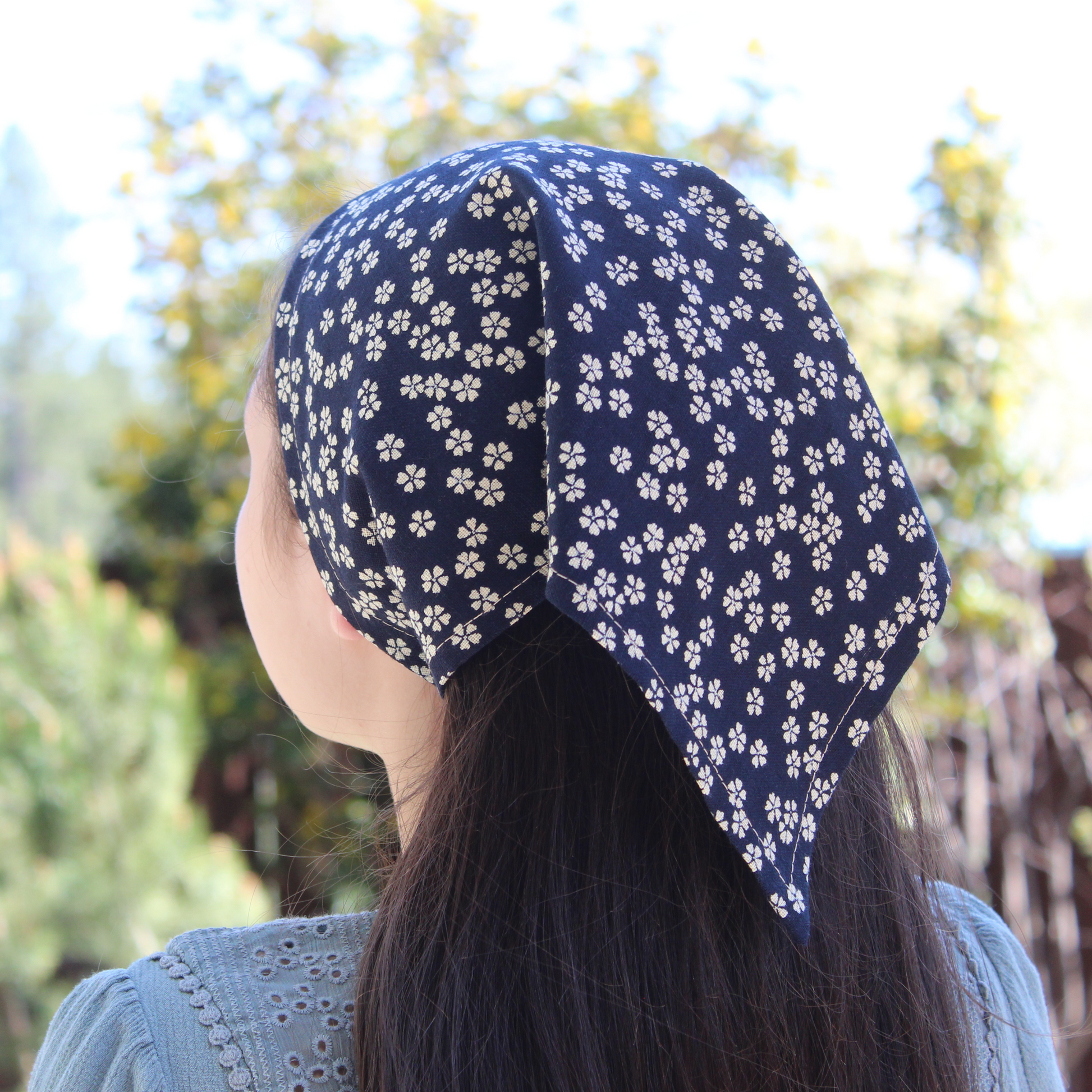 Person wearing a navy blue headscarf with white floral pattern outdoors